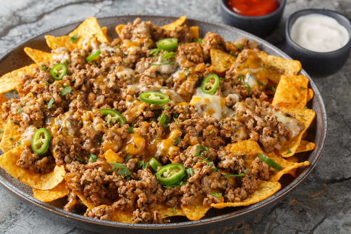 Corn nachos with lots of stewed minced meat, cheddar cheese and jalapeno pepper served with sauces closeup on the plate. Horizontal